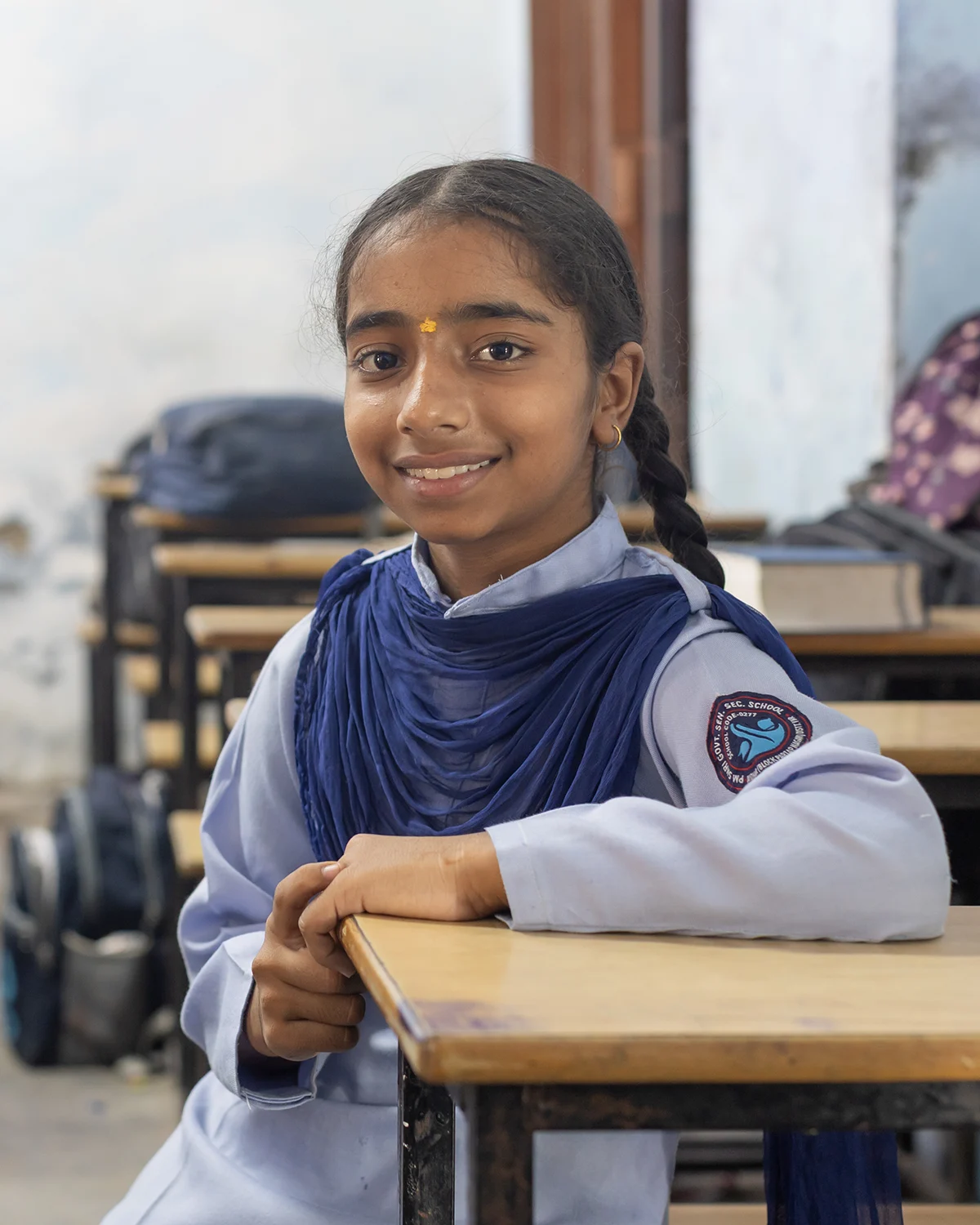 Preeti sits at a classroom desk, smiling.