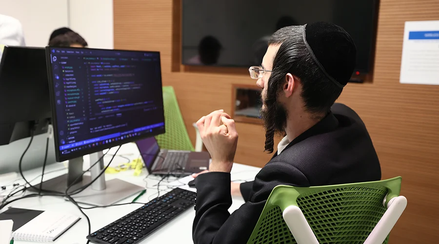 A young Jewish man codes on a computer in a lab.