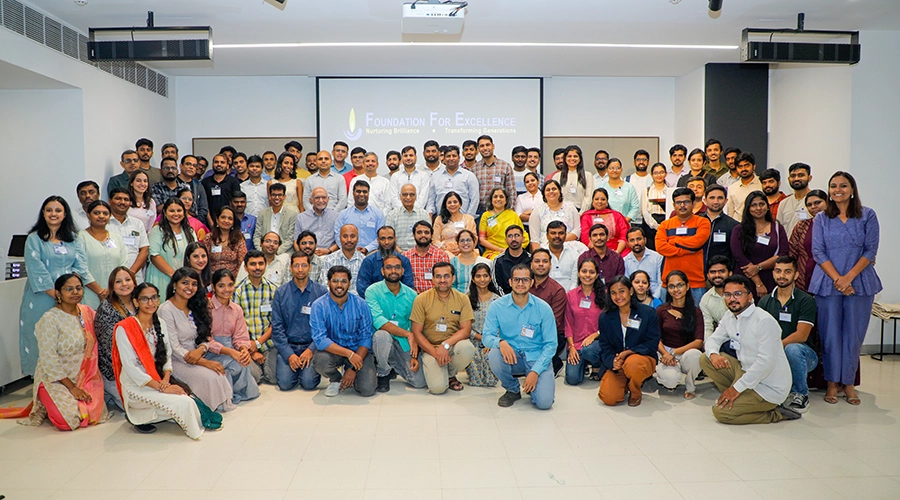 A group of Foundation for Excellence (FFE) participants stand together, smiling in classroom.