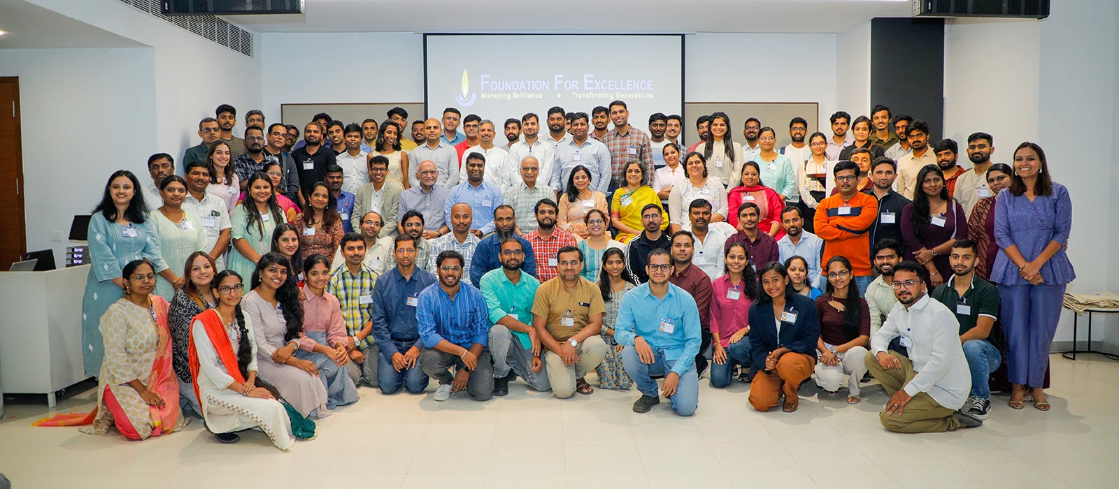A group of Foundation for Excellence (FFE) participants stand together, smiling in classroom.