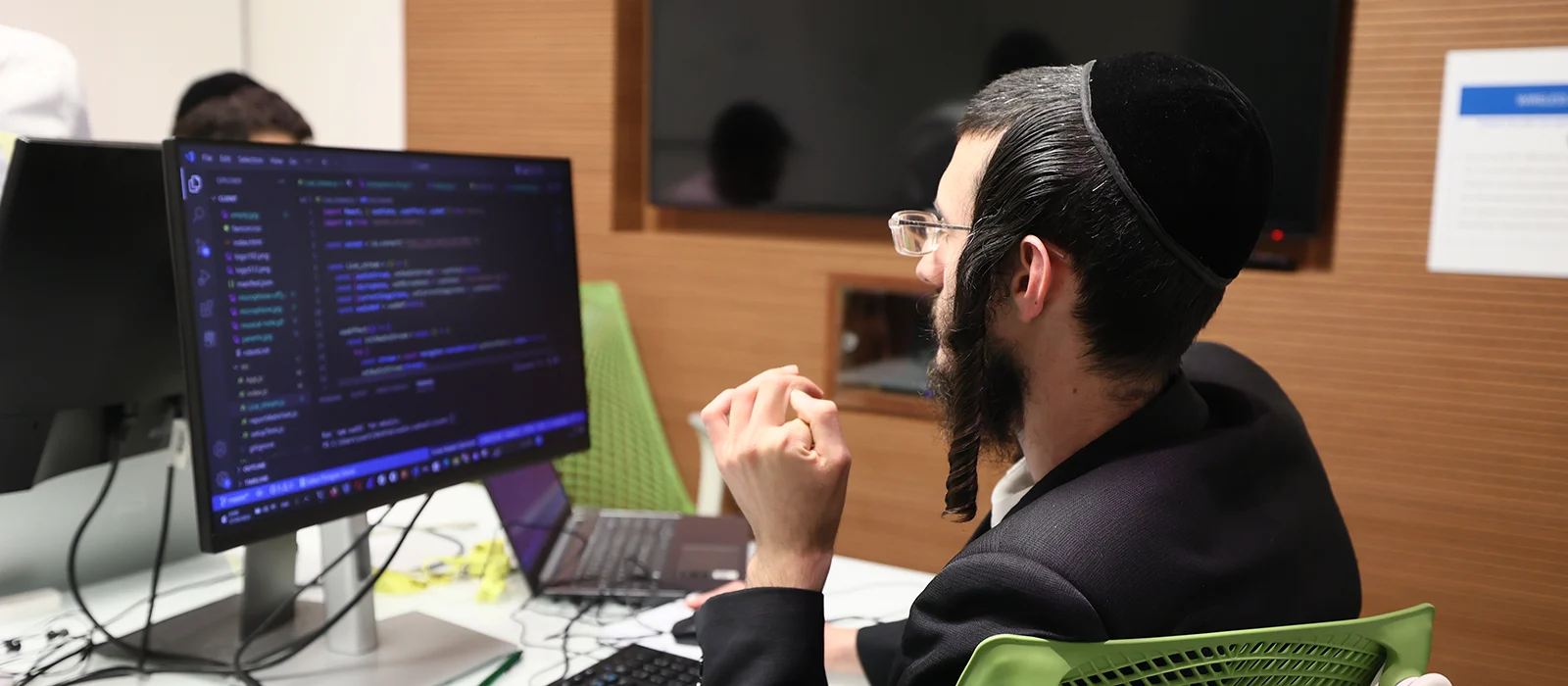 A young Jewish man codes on a computer in a lab.