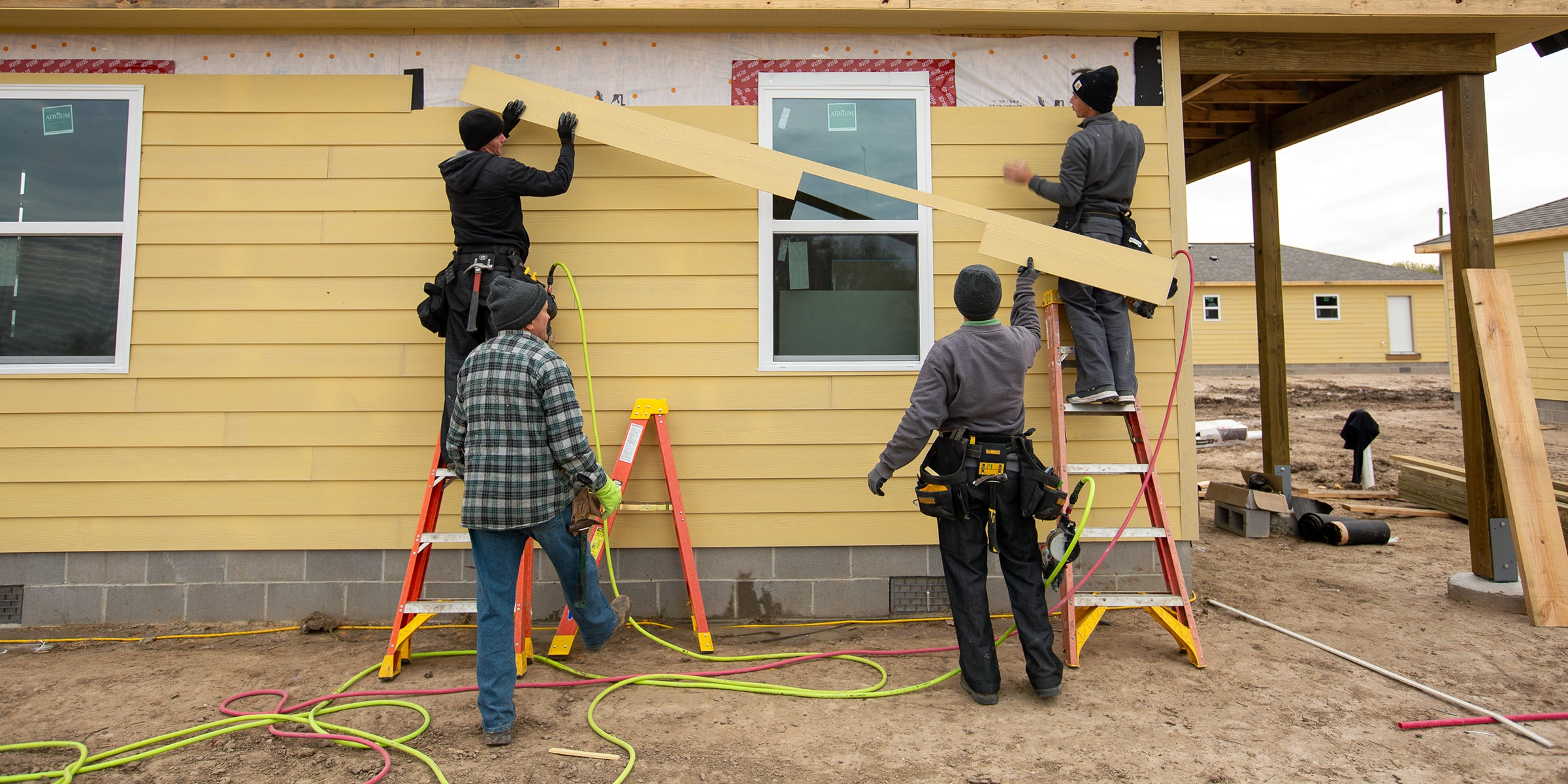 Four people attach siding to a newly rebuilt house.