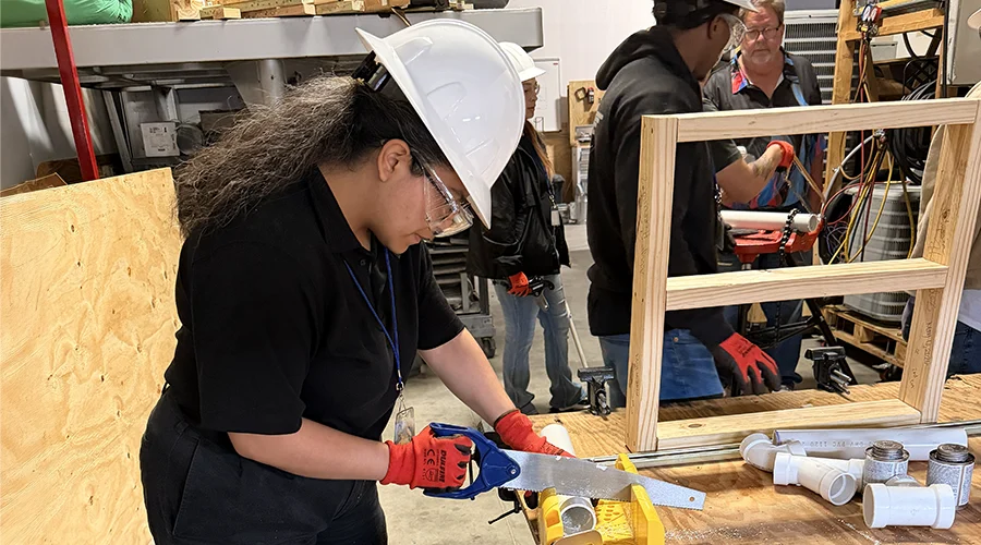 A young woman uses a saw during training.