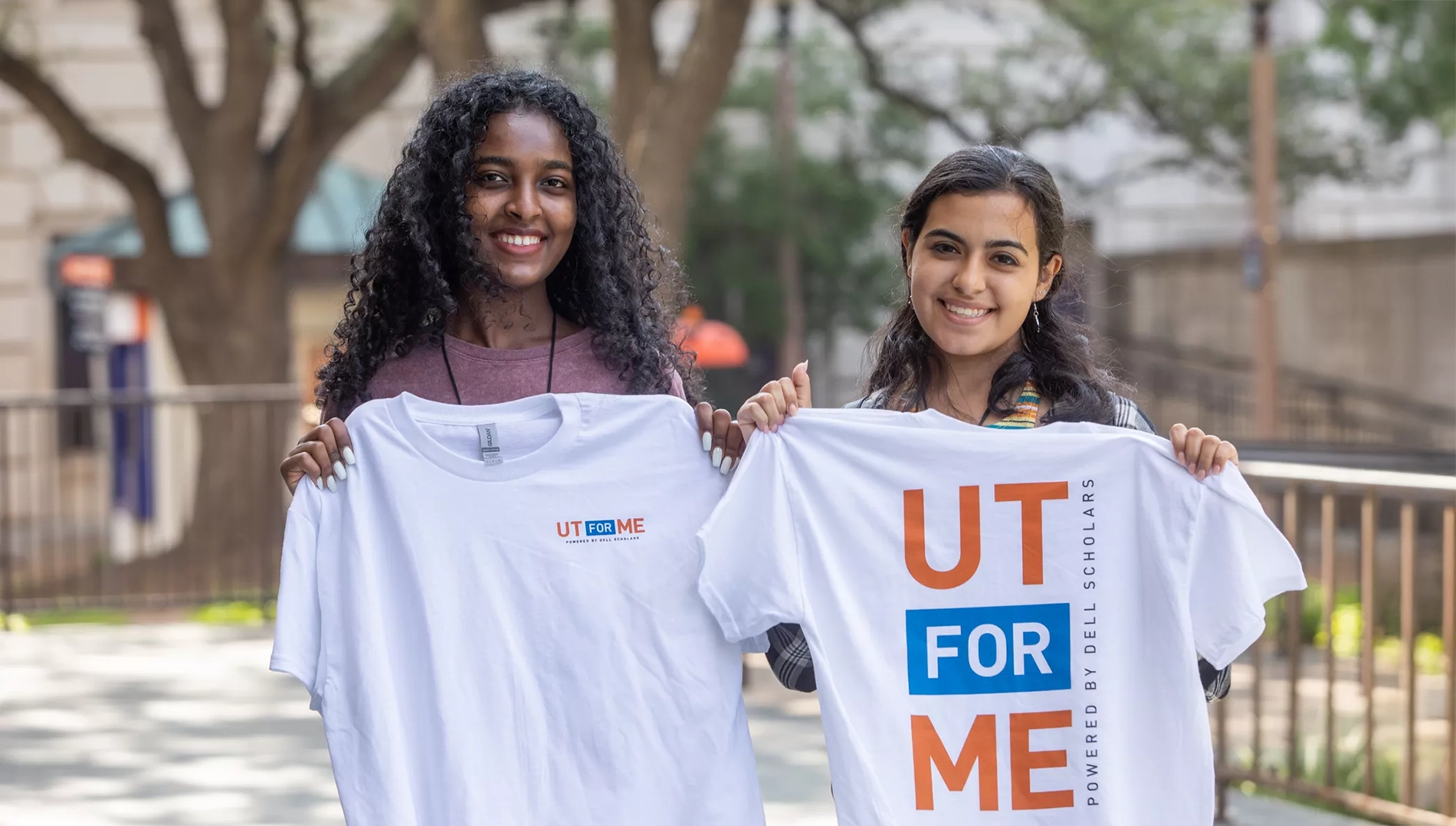 Two smiling students hold "UT for Me" t-shirts.