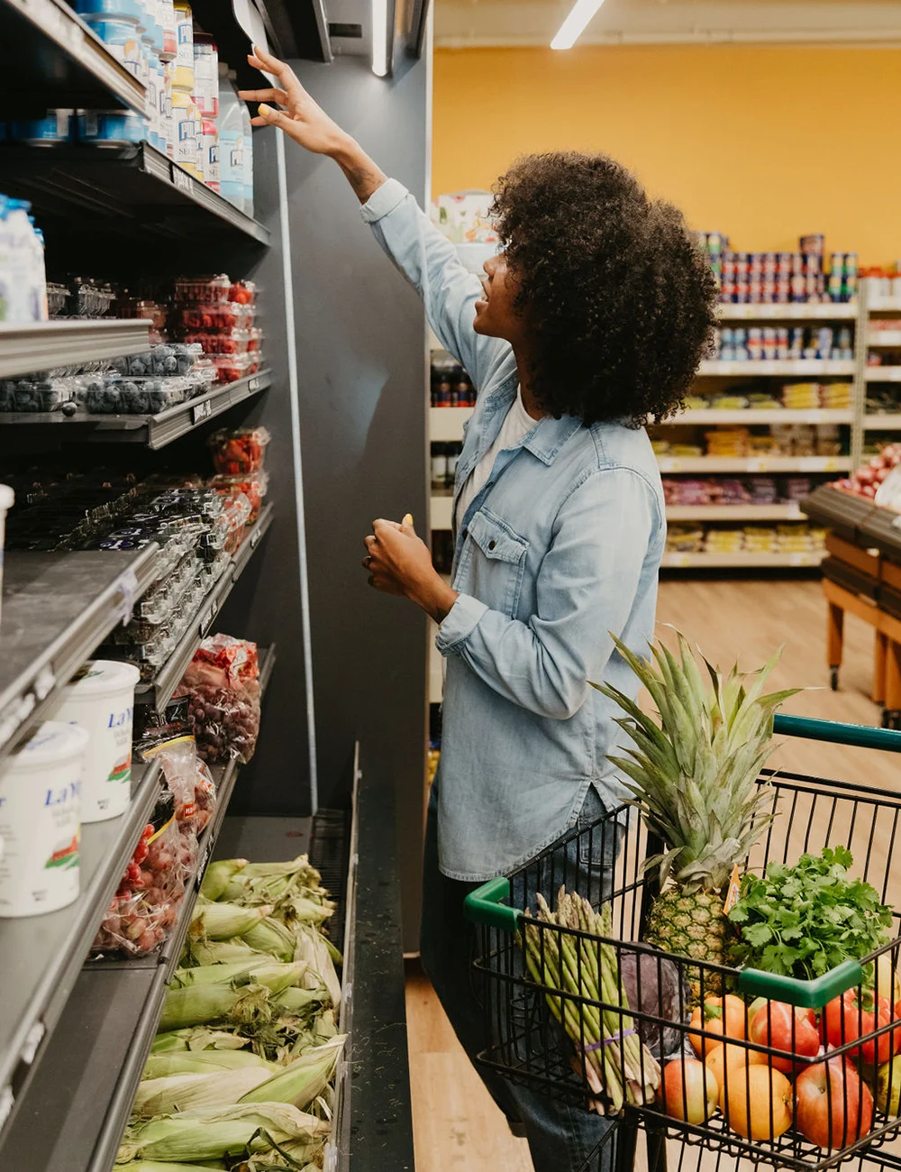A shopper reaches for an item on the shelf in the grocery store produce aisle.
