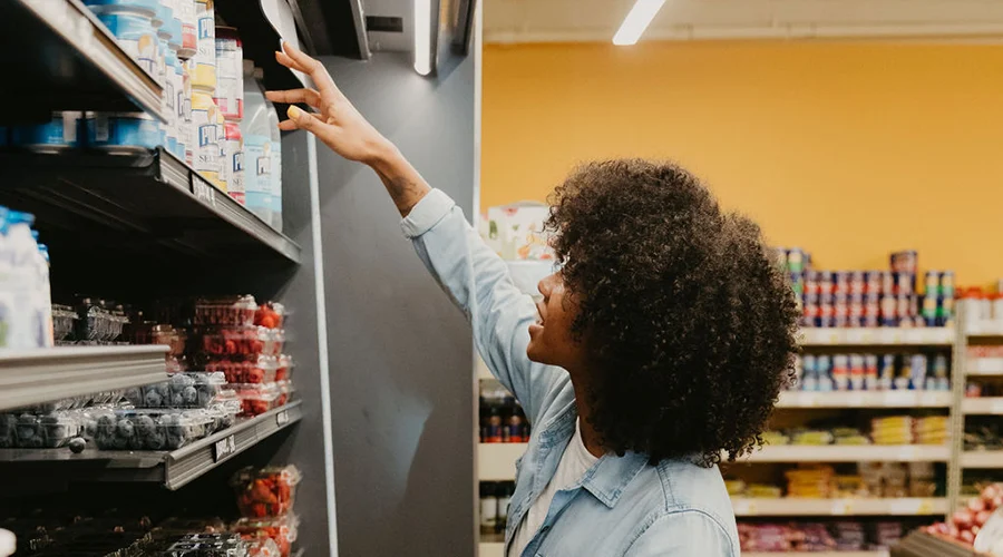 A shopper reaches for an item on the shelf in the grocery store produce aisle.