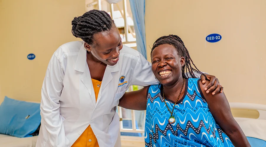 A doctor hugs a smiling patient as she sits on a hospital bed.