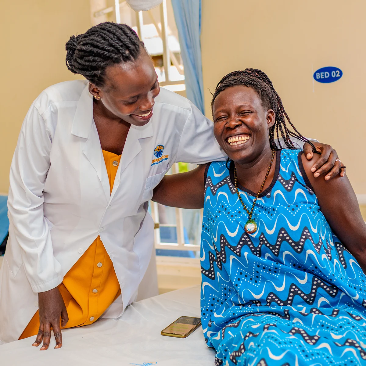 A doctor hugs a smiling patient as she sits on a hospital bed.