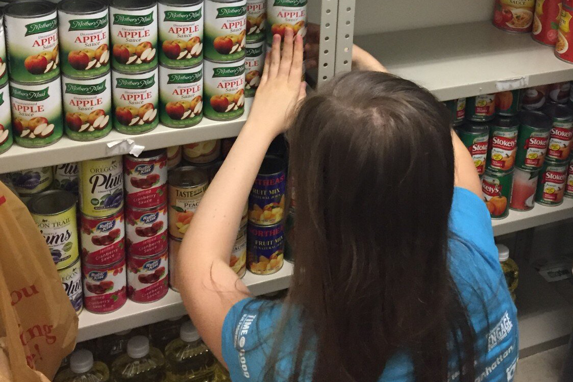 A woman stocks a pantry shelf with food cans.