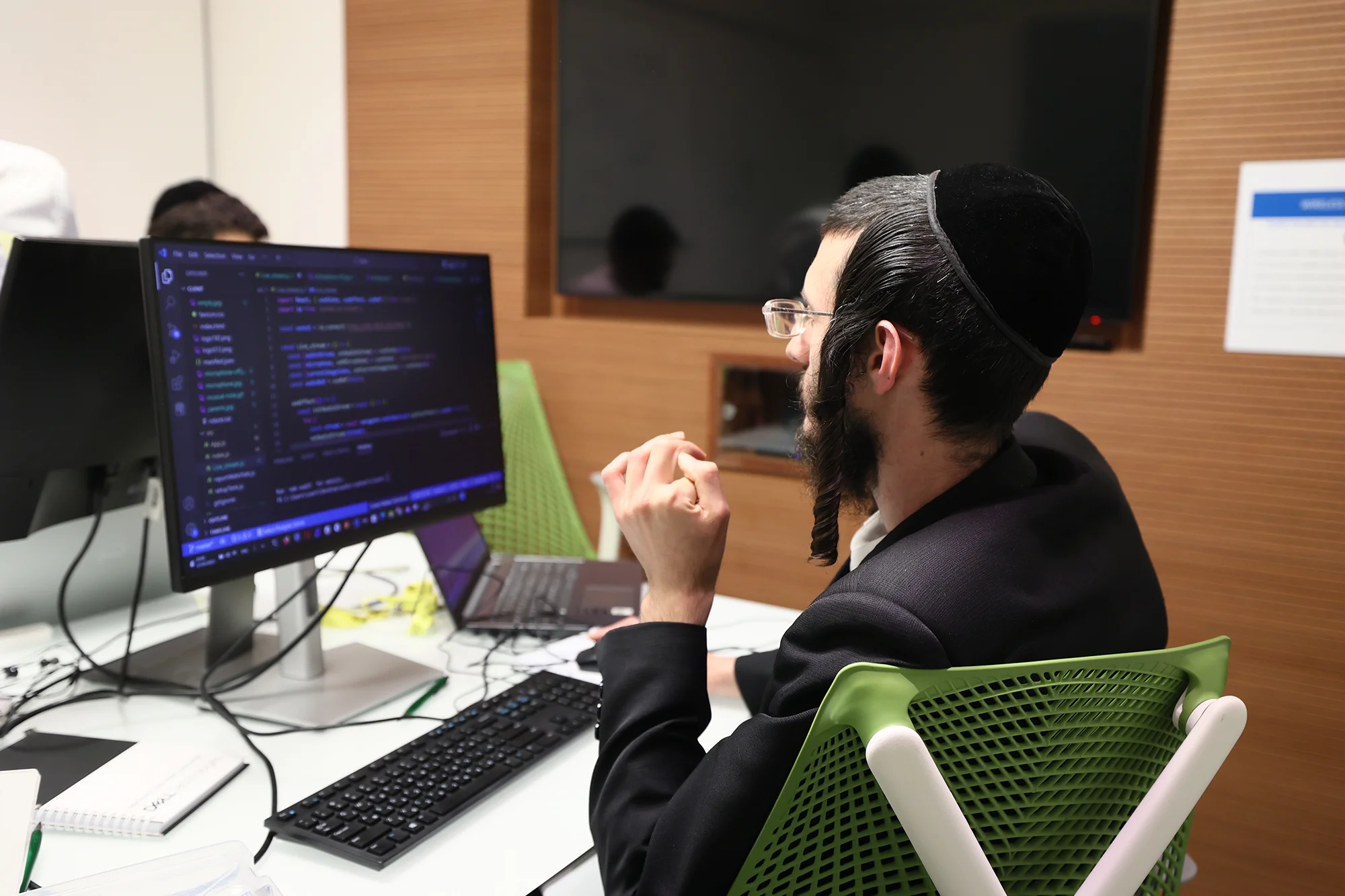A young Jewish man codes on a computer in a lab.