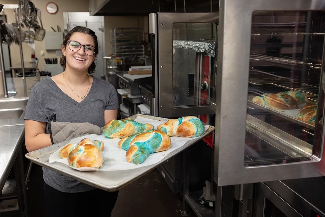 A woman holds a pan of freshly baked challah while standing in a kitchen.