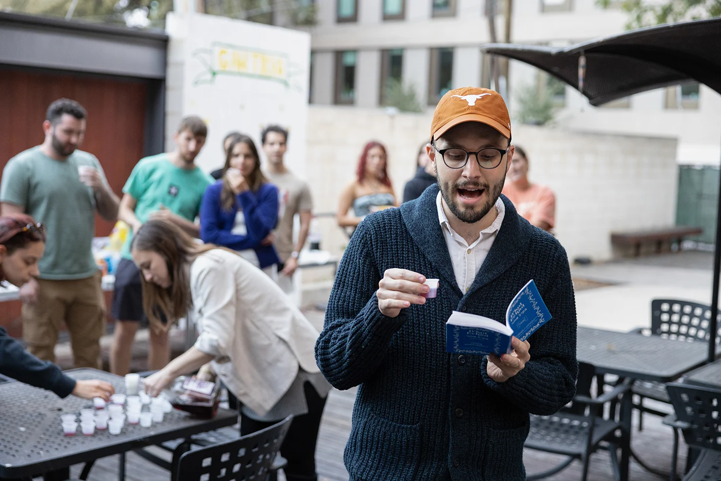 A student in a burnt orange Longhorns hat reads aloud at a Yom Kippur pre-fast event at Texas Hillel on campus.