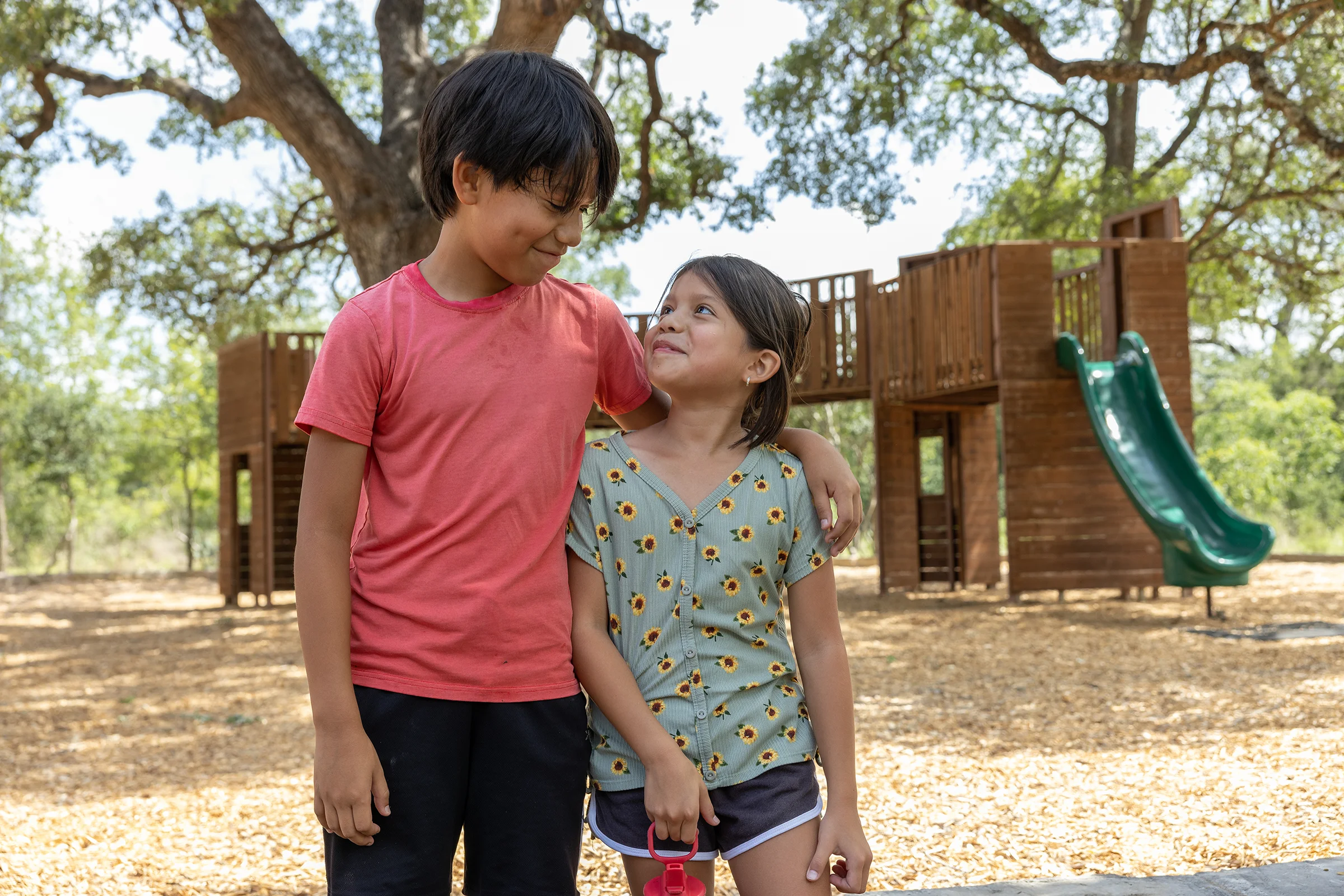 A pair of children smile at each other on a playground.