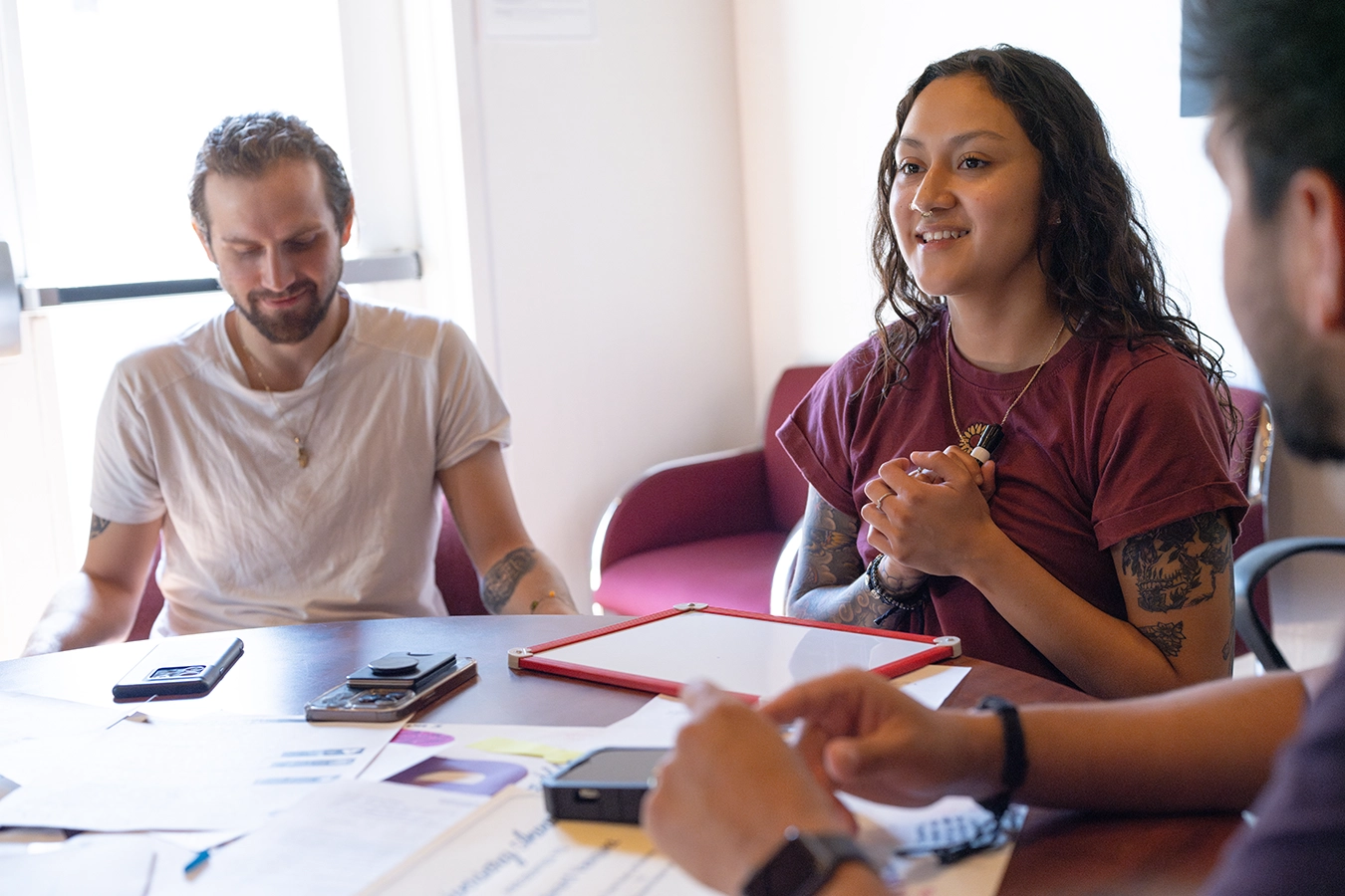 Three people sit a conference room table in a meeting.